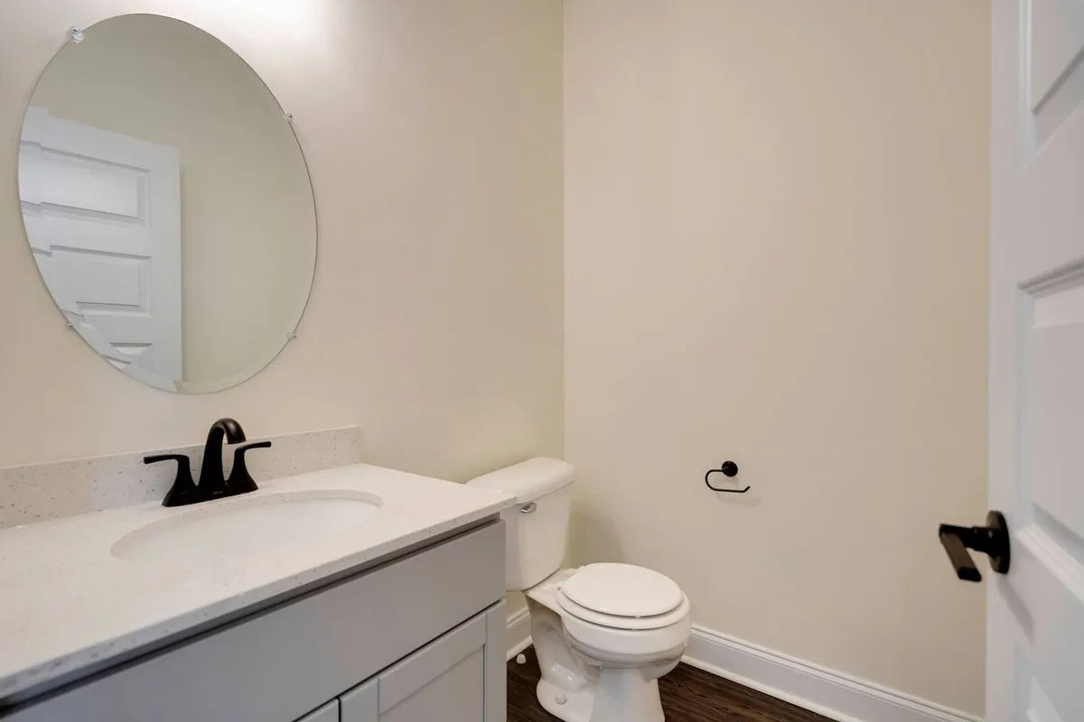 A minimalist powder room with a round mirror, contemporary sink, and toilet. The uncluttered design and calming mood make it a practical and stylish addition for guests' convenience.