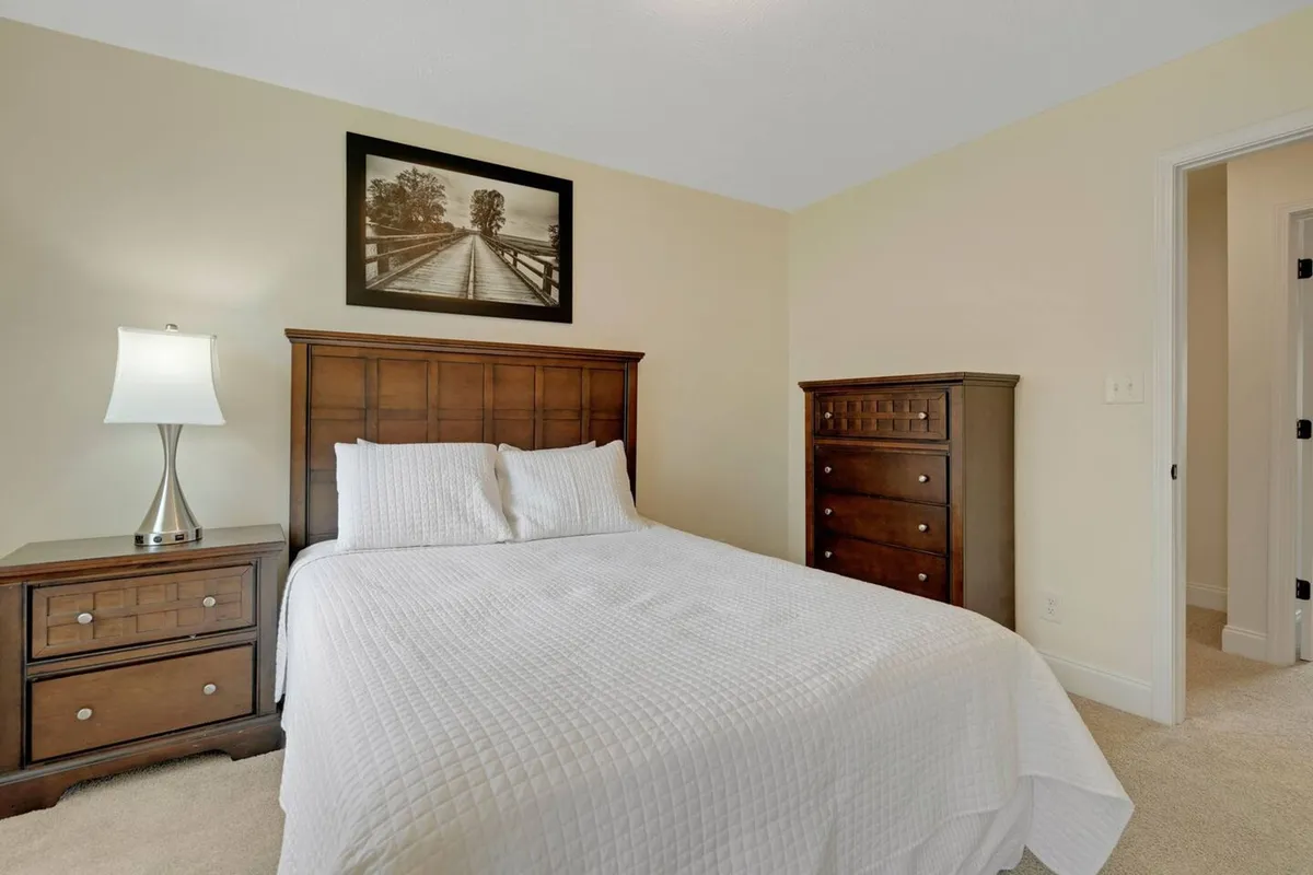 A serene bedroom setup featuring a made bed, nightstand with lamp, chest of drawers, and tasteful wall art, all arranged to feel peaceful and functional.