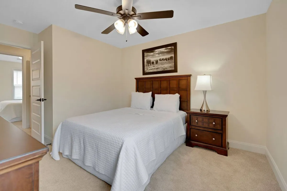 A warmly lit bedroom featuring a bed with a white quilt, a wooden headboard, a nightstand with a lamp, and framed artwork on the wall. The setting feels inviting and comfortable, illustrating a ready-to-use sleeping space.