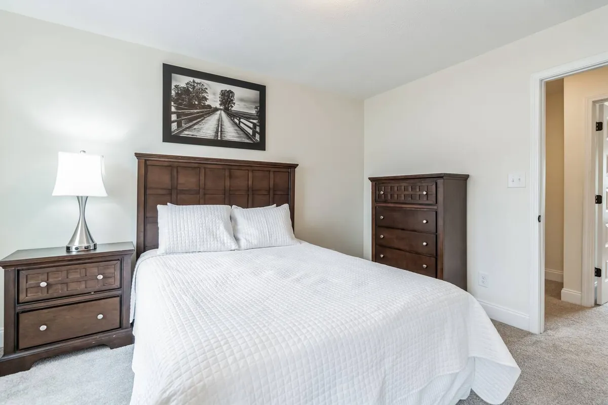 A serene bedroom featuring a made bed with plush bedding, a nightstand with a softly glowing lamp, and framed artwork above, all illuminated by gentle natural light. The overall atmosphere is tranquil and inviting, with thoughtful decor designed for relaxation.