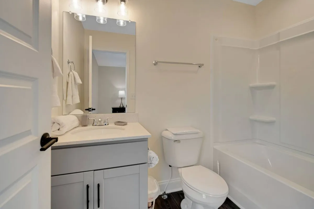A bright and modern bathroom with a vanity sink, large mirror, toilet, and bathtub. The clean lines and inviting atmosphere make it an ideal space for refreshing morning routines or unwinding with a relaxing bath in the evening.